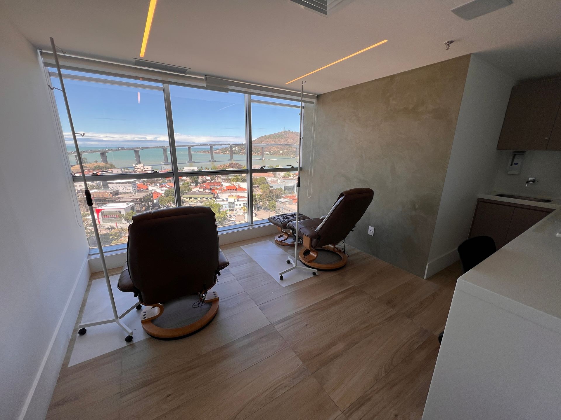 Modern waiting room with recliner chairs and large windows overlooking a cityscape with a bridge.
