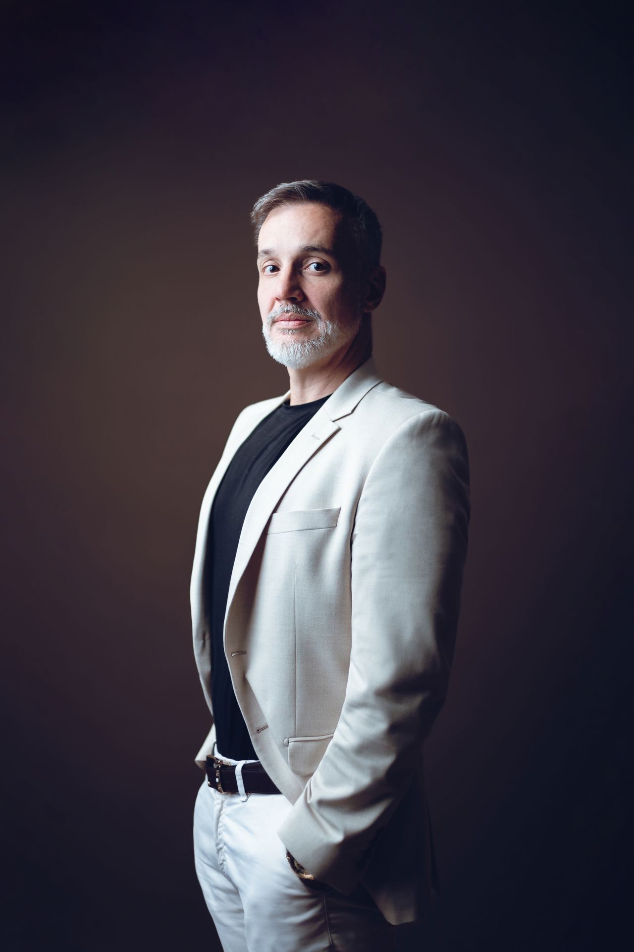 Man in a beige suit jacket poses confidently against a dark background.